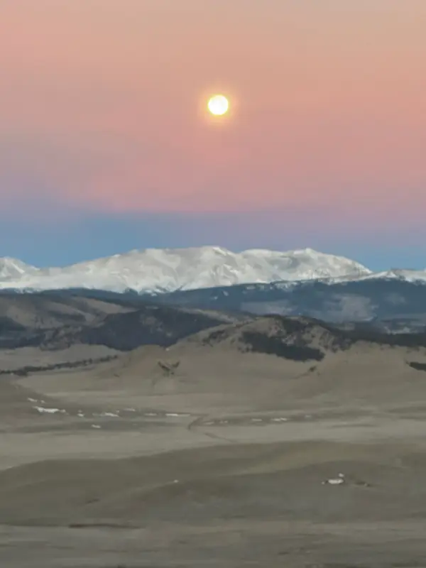 Moonrise in a rose-colored sky above the mountains
